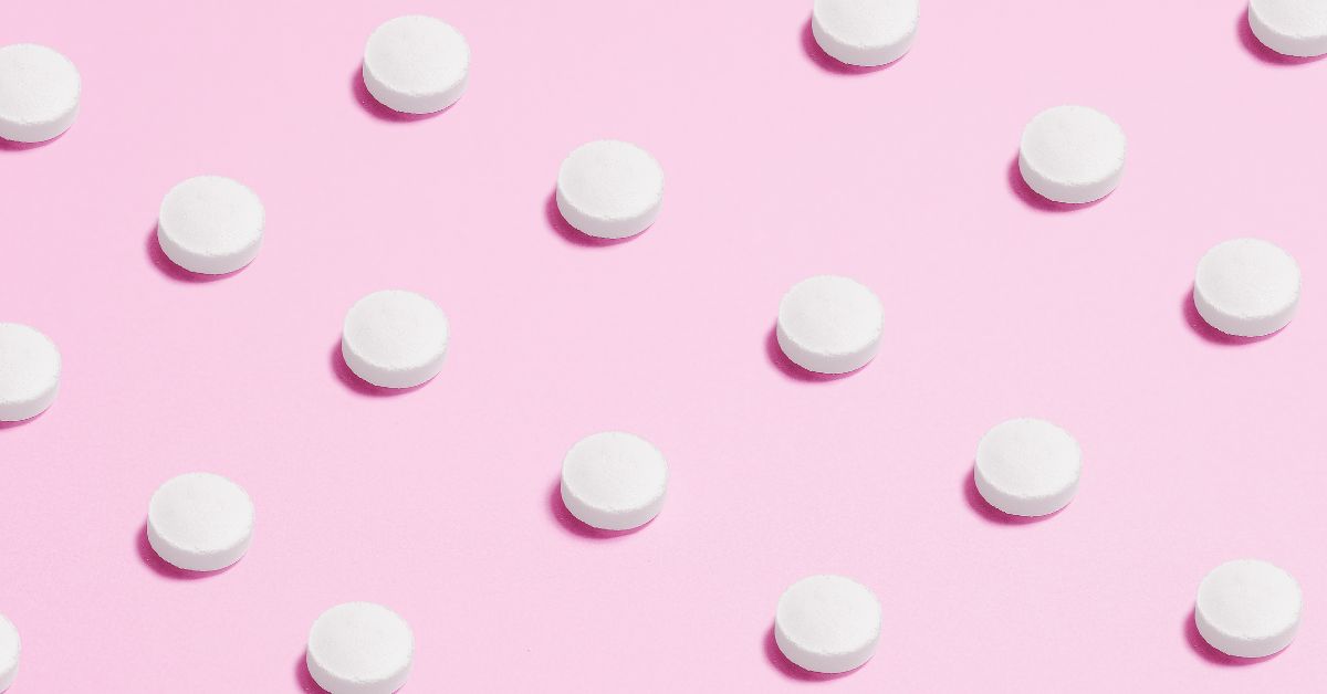 A photo of small white tablets spread out in an even pattern on a pink background