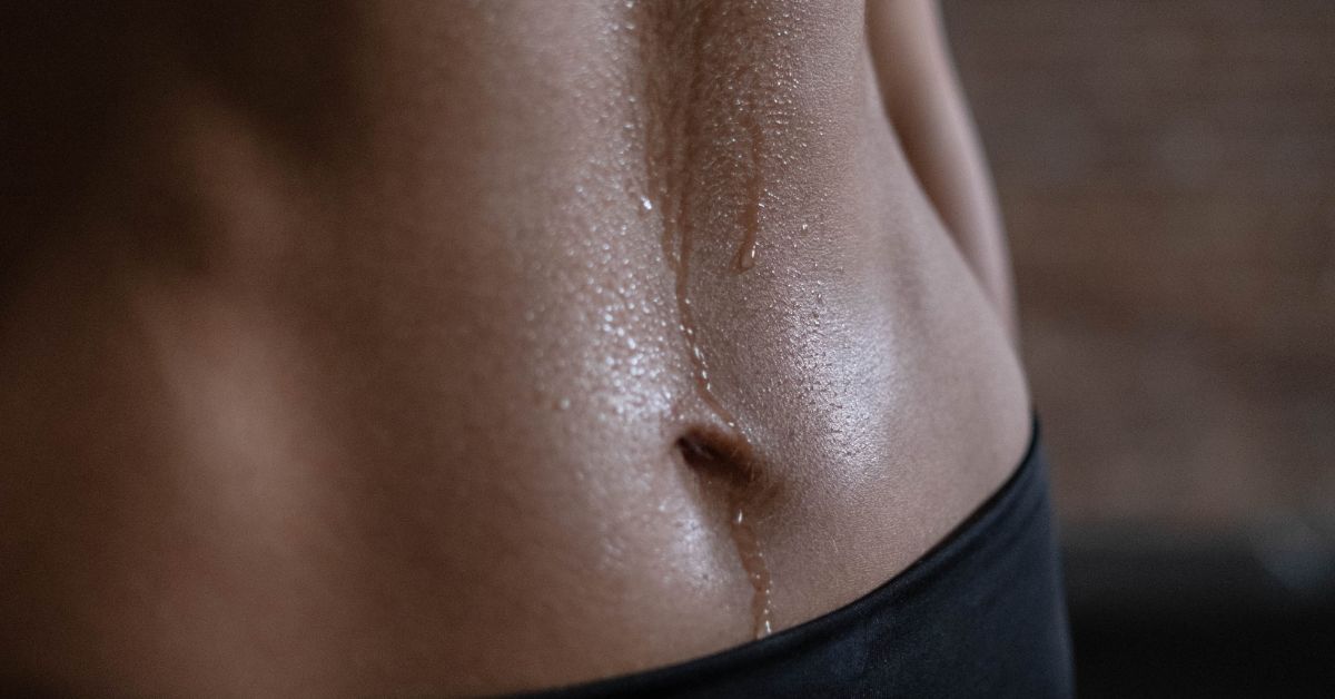 Close-up image of a woman's abdominal section showing some sweat and workout wear.